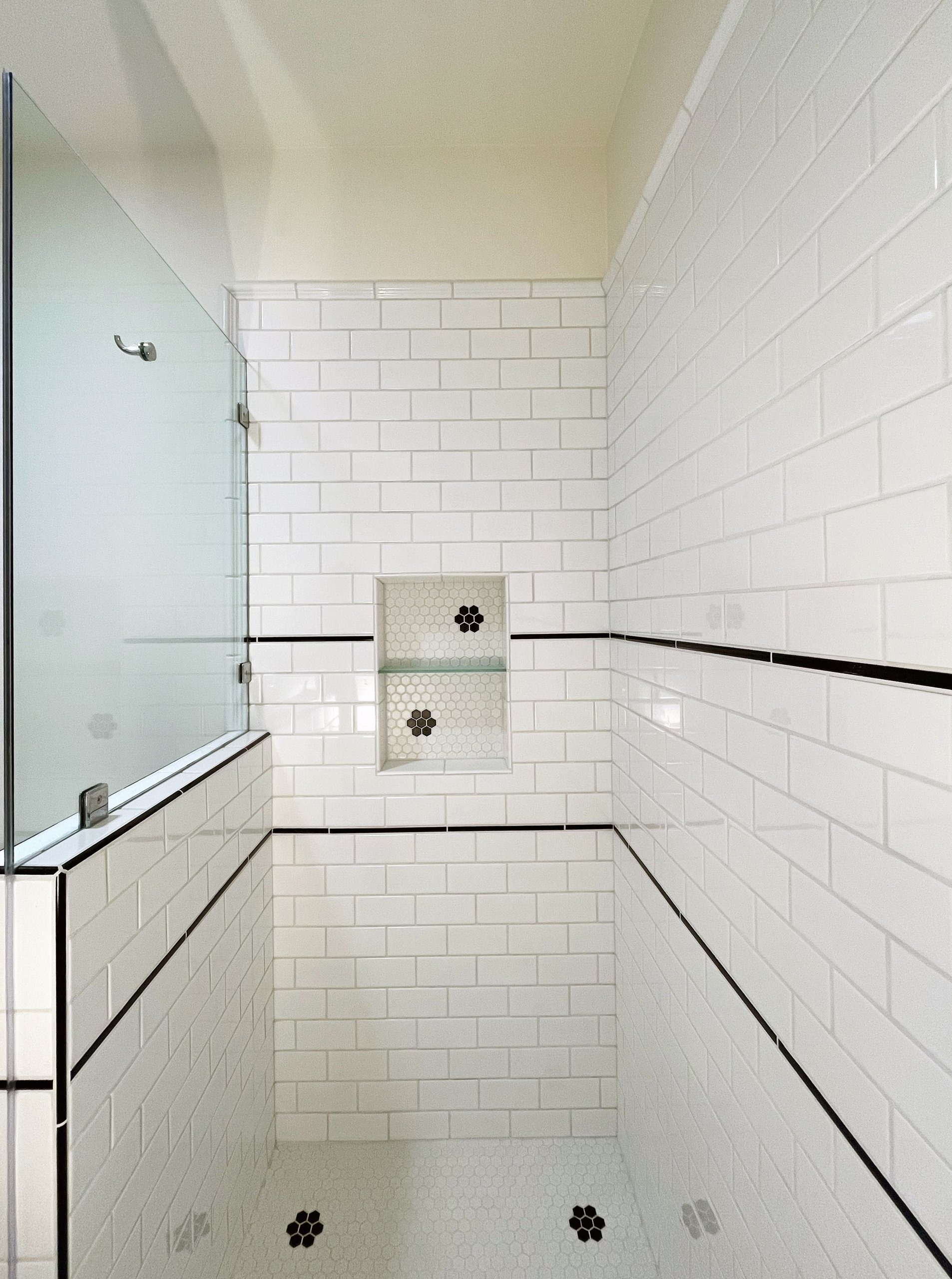 White subway tile shower with black pencil trim and hex mosaic flower accents in the niche and floor