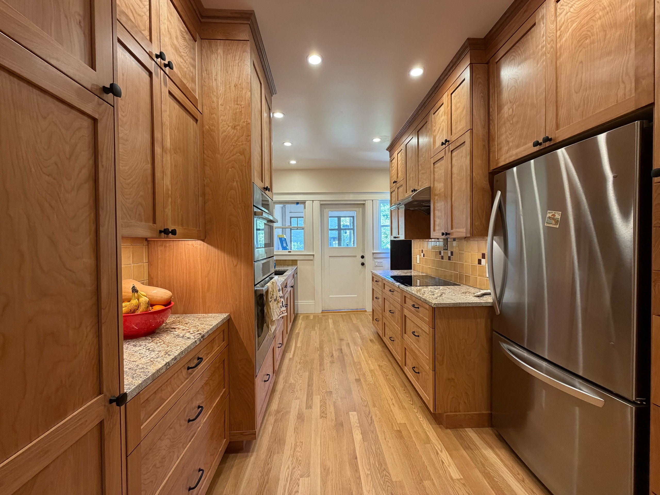 Remodeled galley kitchen with wood cabinetry, granite counters, and oak floors