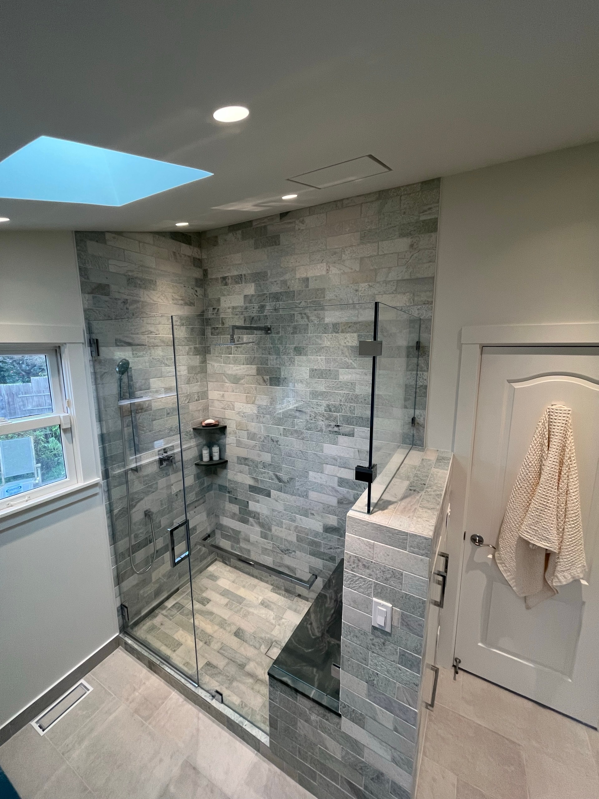 Walk-in shower with gray stone subway tile, glass panel, and tiled bench