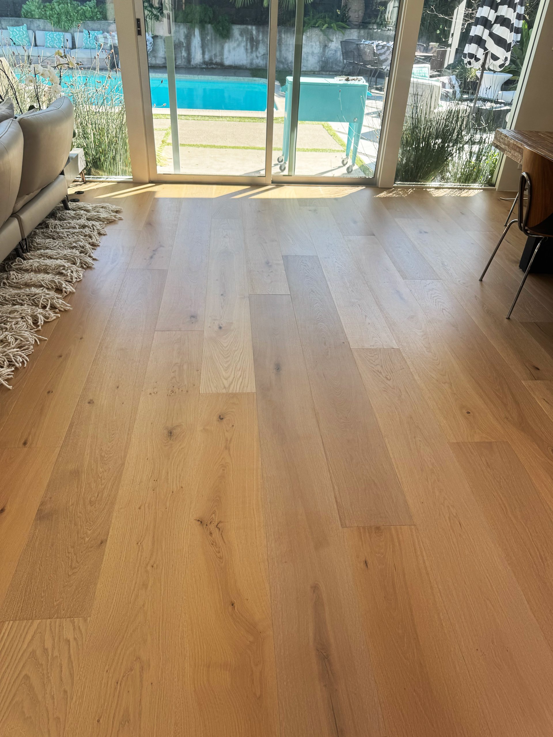 Wide plank oak flooring in a bright living room with sliding glass doors to a pool