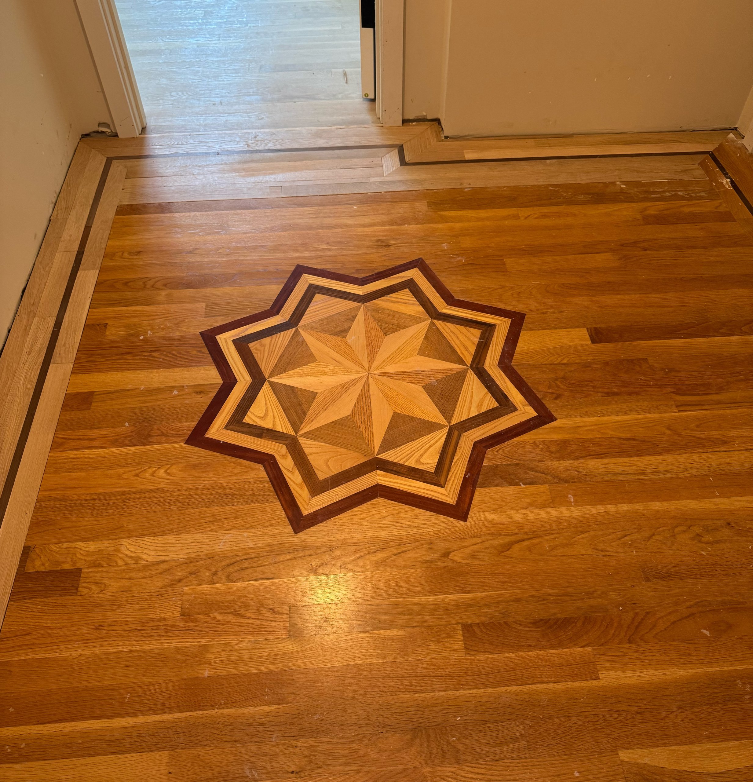 Hardwood floor with an inlaid eight point star medallion and a hand laid border following the walls