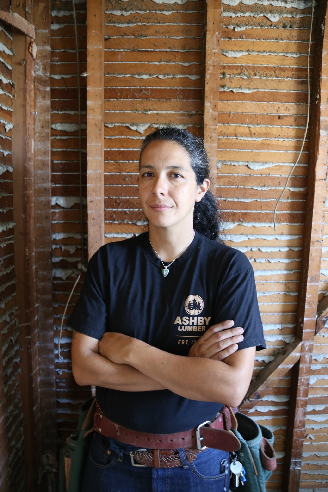 Jess Salgado, owner of Four Winds Construction, in a tool belt in front of an open stud wall